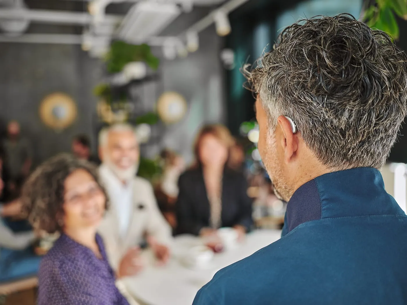 Homem usando aparelho auditivo conversando com um grupo de amigos à mesa