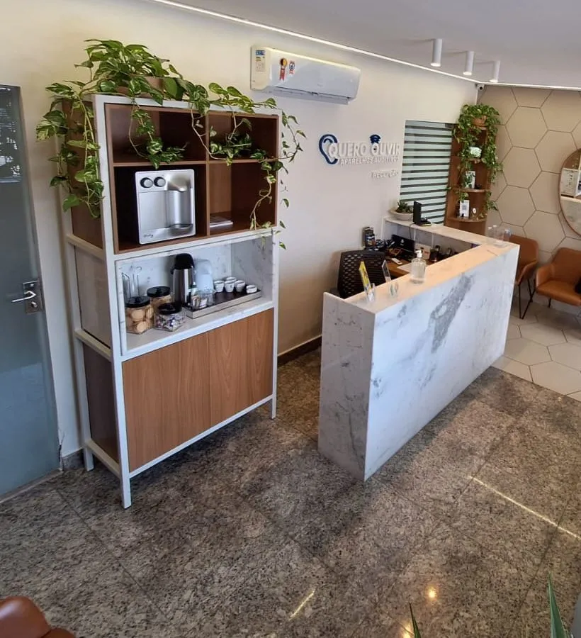 Recepção da Quero Ouvir em Goiânia, com balcão de mármore, café e plantas